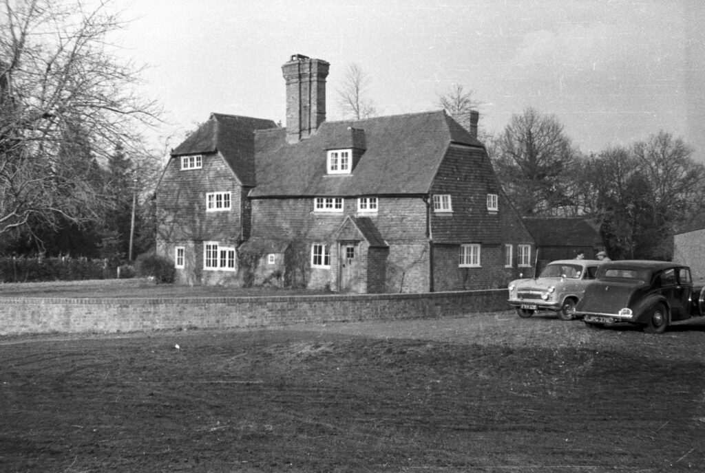 Old B&W image of a farmhouse and cars.
