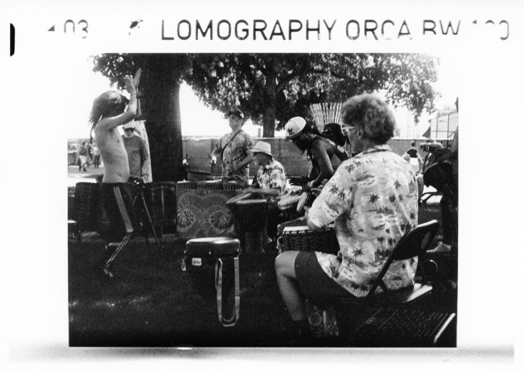 Black and white photo of a drum circle in a park with a shirtless male dancer