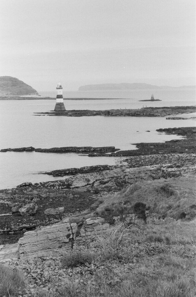 A view of a lighthouse at low tide with mountains, coastline and sea visible.