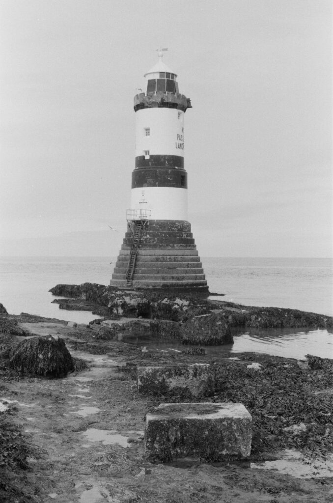 Small lighthouse at low tide with rocks and a causeway leading to it in the foreground.