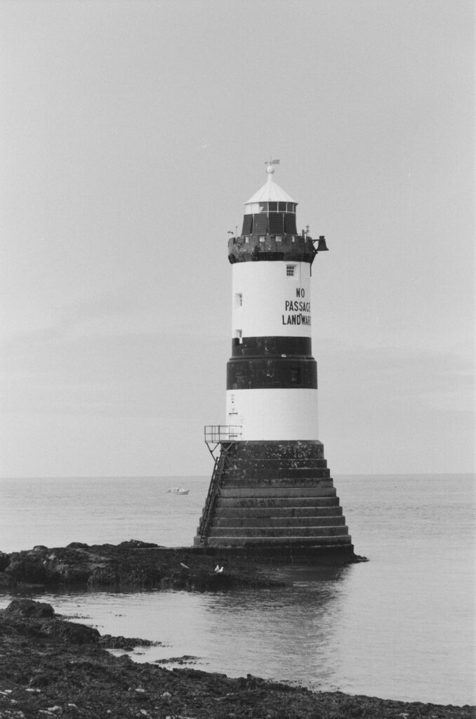 A small lighthouse with black and white horizontal stripes on rocks at low tide.
