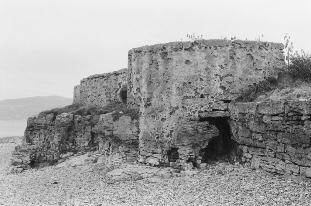 A pebbly beach with a badly eroded concrete wall at its edge