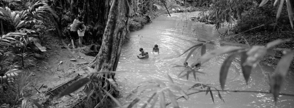 Kids playing in buckets in the river in the Philippines in between trees in black and white