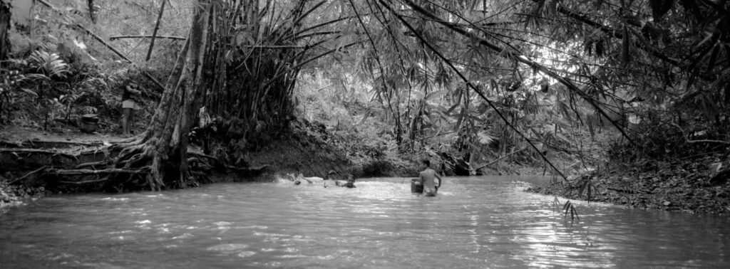 Kids playing in buckets in the river in the Philippines in between trees in black and white