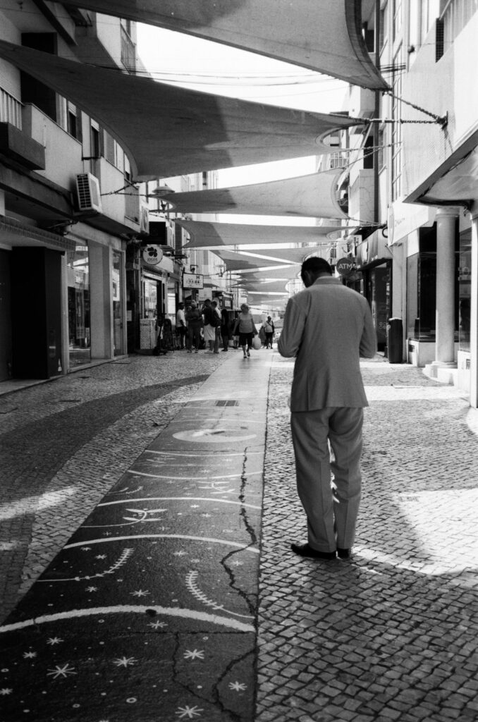 b&w photo of a man in a suit checking his phone on the main commercial street in Portimao