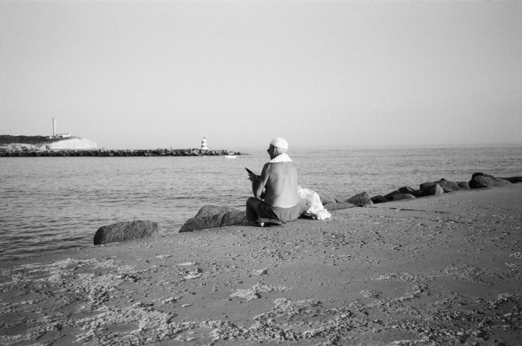 b&w photo of a man sitting on the pier at Praia da Rocha packing away his fishing rod