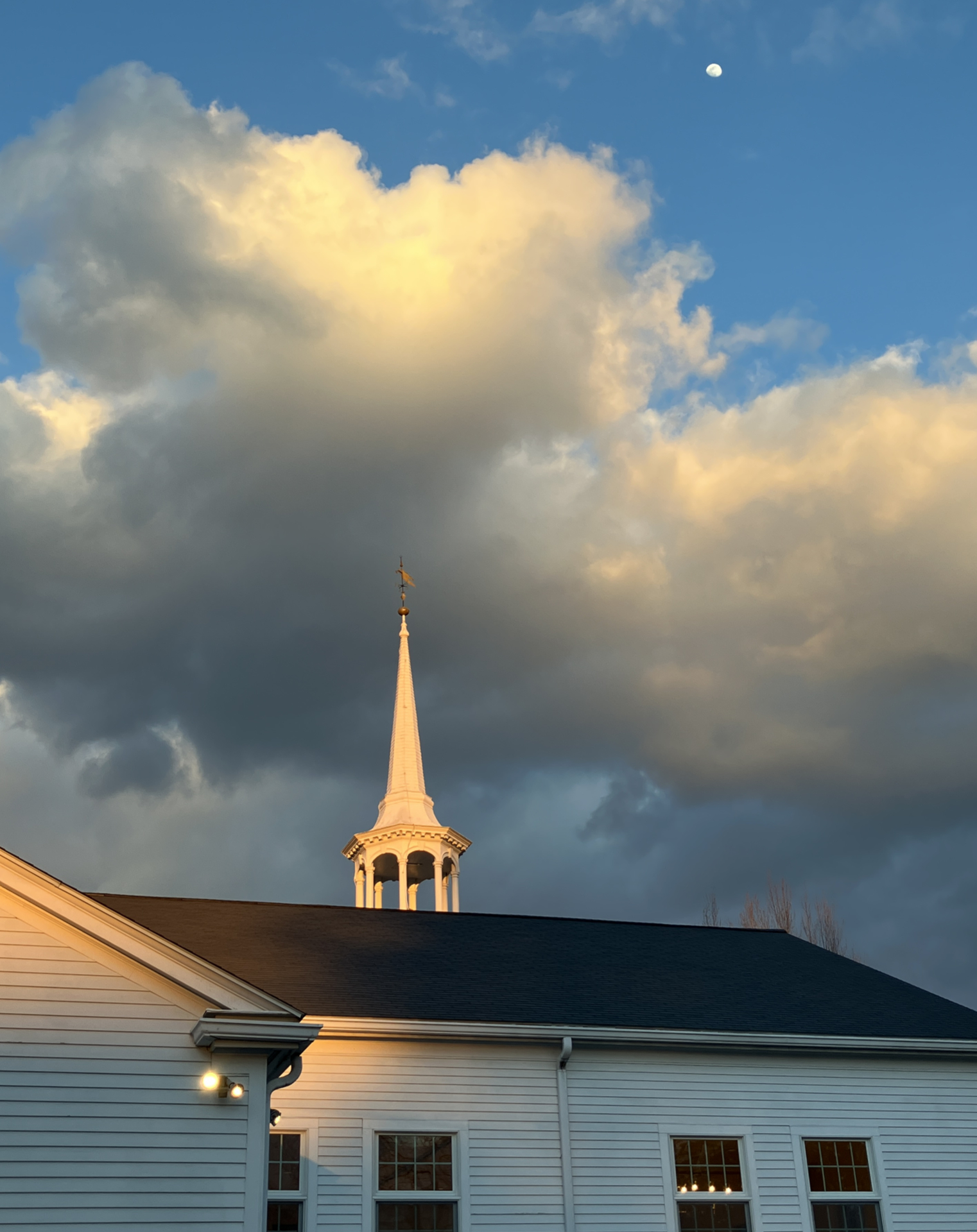 Sunset light grazing a church roof, steeple, clouds and then reflecting off the moon
