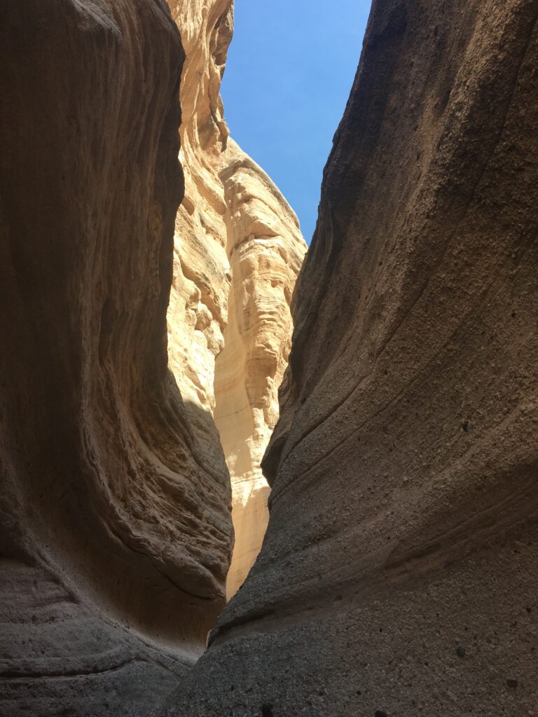 view of a sliver of blue sky looking up through a narrow brown rocky slot canyon