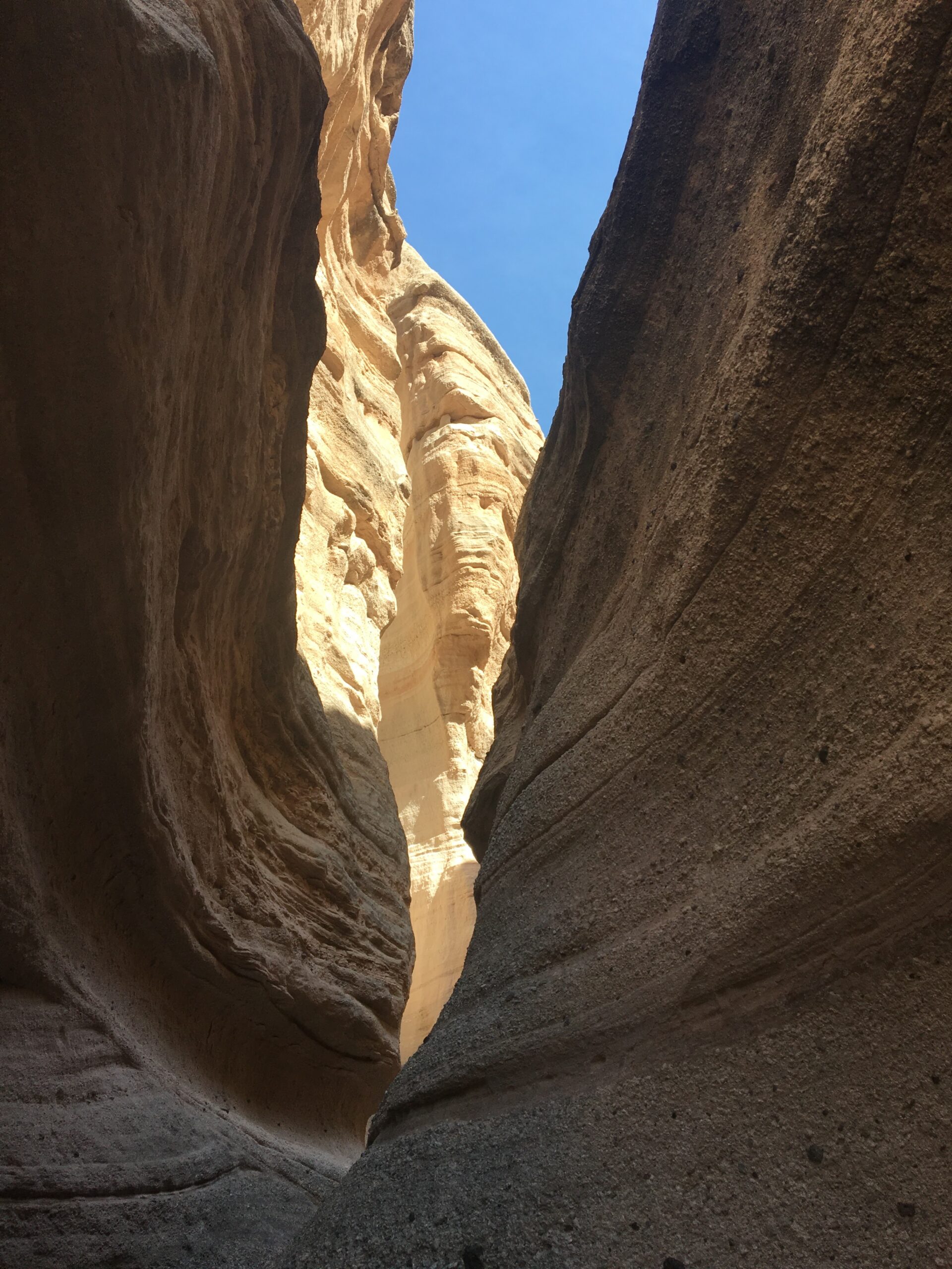 view of a sliver of blue sky looking up through a narrow brown rocky slot canyon