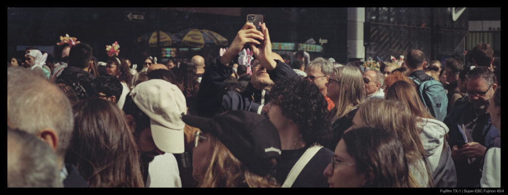 A person stands side-on to a crowd, raising their phone to take a picture.