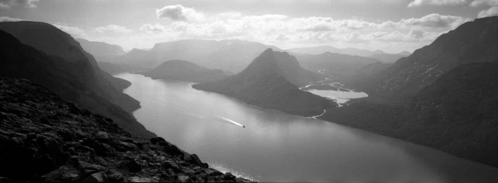 A view from Besseggen in Norway in black and white, with a tiny boat going through the fjord