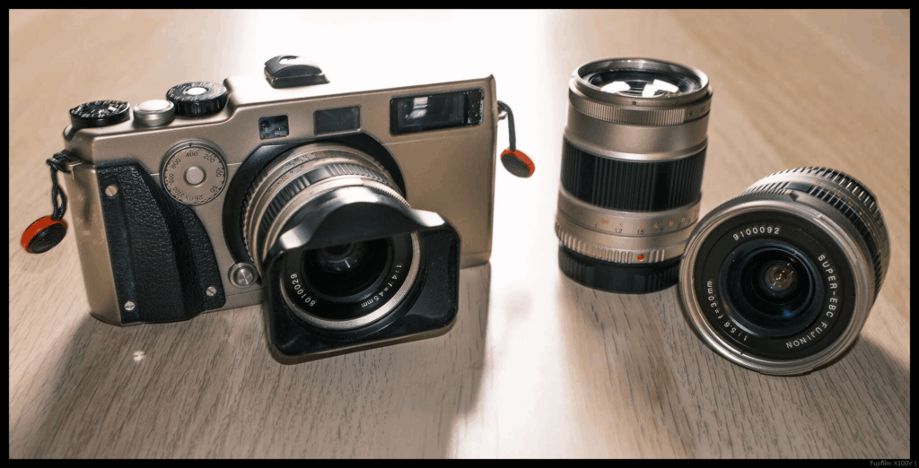 An image of a Fujifilm TX-1 with the 45/4 mounted sitting on a table, with a 90/4 and 30/5.6 placed next to it.