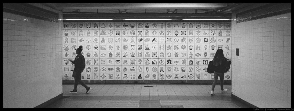 Two people split, walking to the left and right around corners of a split subway station.