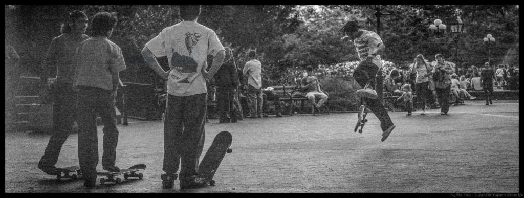 An image of a skateboarder at the apex of a jump, watched by other skateboarders.