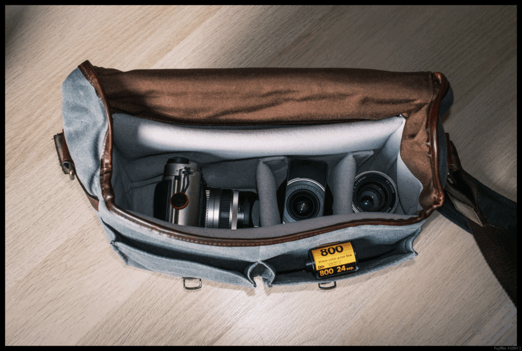 An image of the Fujifilm TX-1 with the 90/4 mounted with both other lenses arranged inside a camera bag from the top.