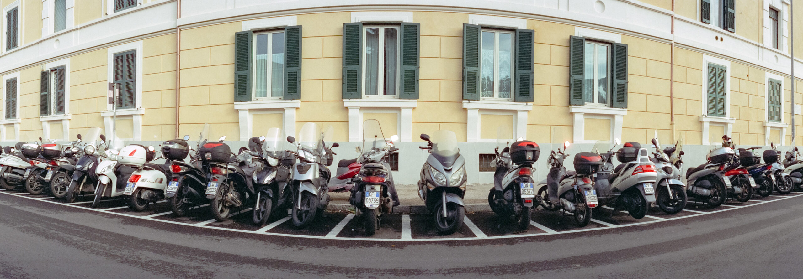 A wide format photo of a row of tightly parked moped motorcycles