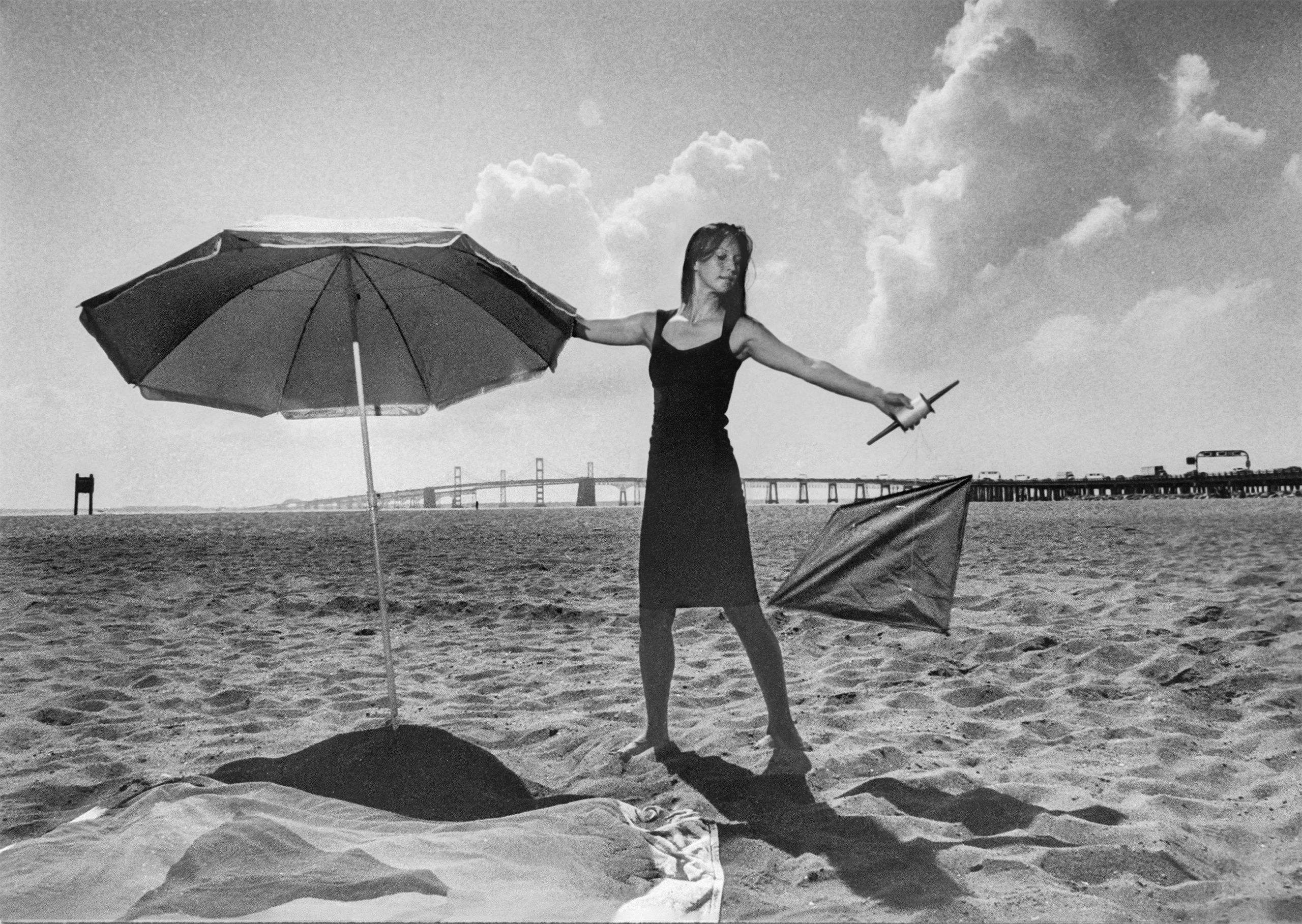 An actor balances a beach umbrella while flying a kite.