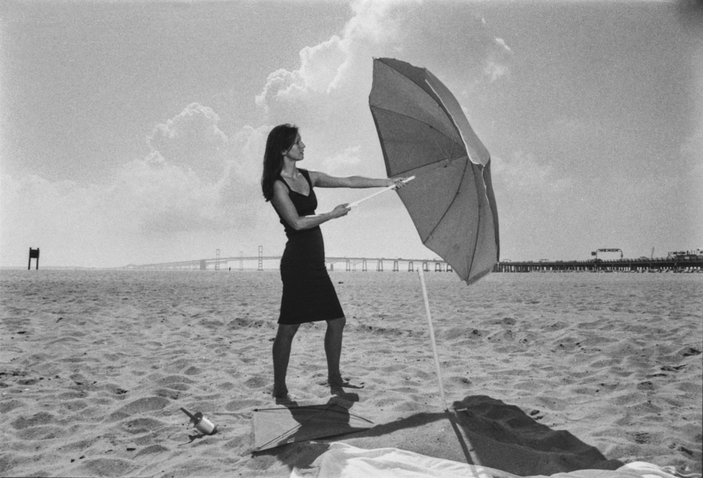 An actor opens an umbrella on a beach.