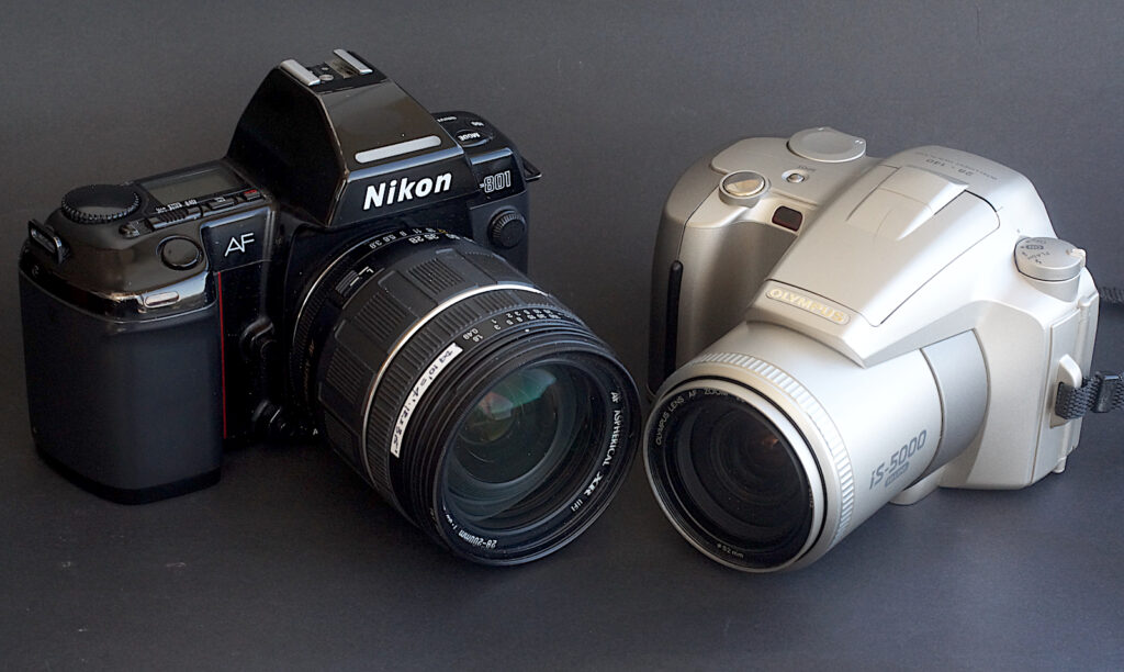 Compared to a Nikon F801 with Tamron 28-200 fitted. The Tamron has an f3.5 maximum aperture and a longer zoom both contributing to its greater bulk. The Nikon also takes AA batteries mounted in the grip.