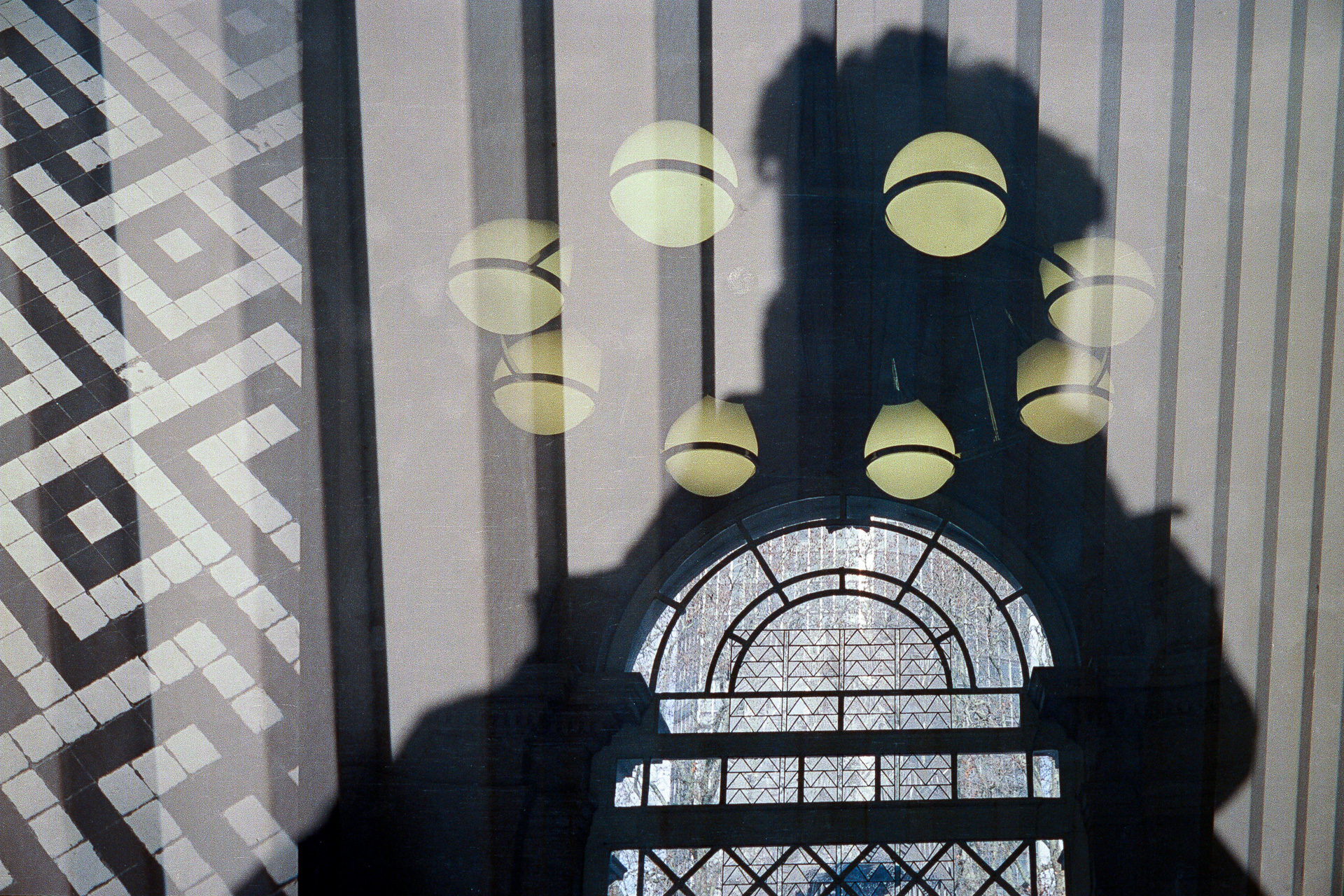 A double exposure featuring a shadow selfie and art deco light fitting and decorative window.