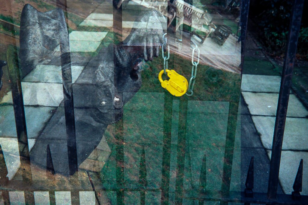 Double exposure on 35mm film featuring a yellow padlock and railings and the sculpture of Becket in the grounds of St Paul's Cathedral. 