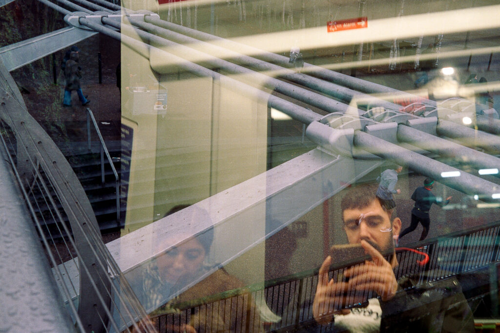 Double exposure featuring two people sitting on a train looking at their phones while runners are jogging over them along viewed from the Millennium Bridge.
