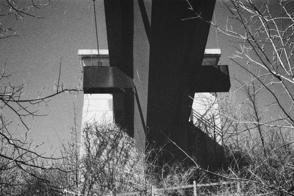A view of a pedestrian bridge from underneath with brush in the foreground.