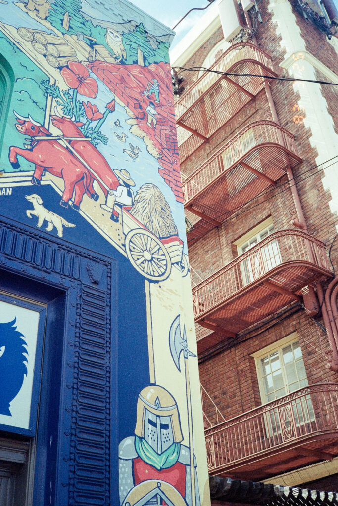 Photo of a mural on the left side and the fire escape on a brick building on the right side