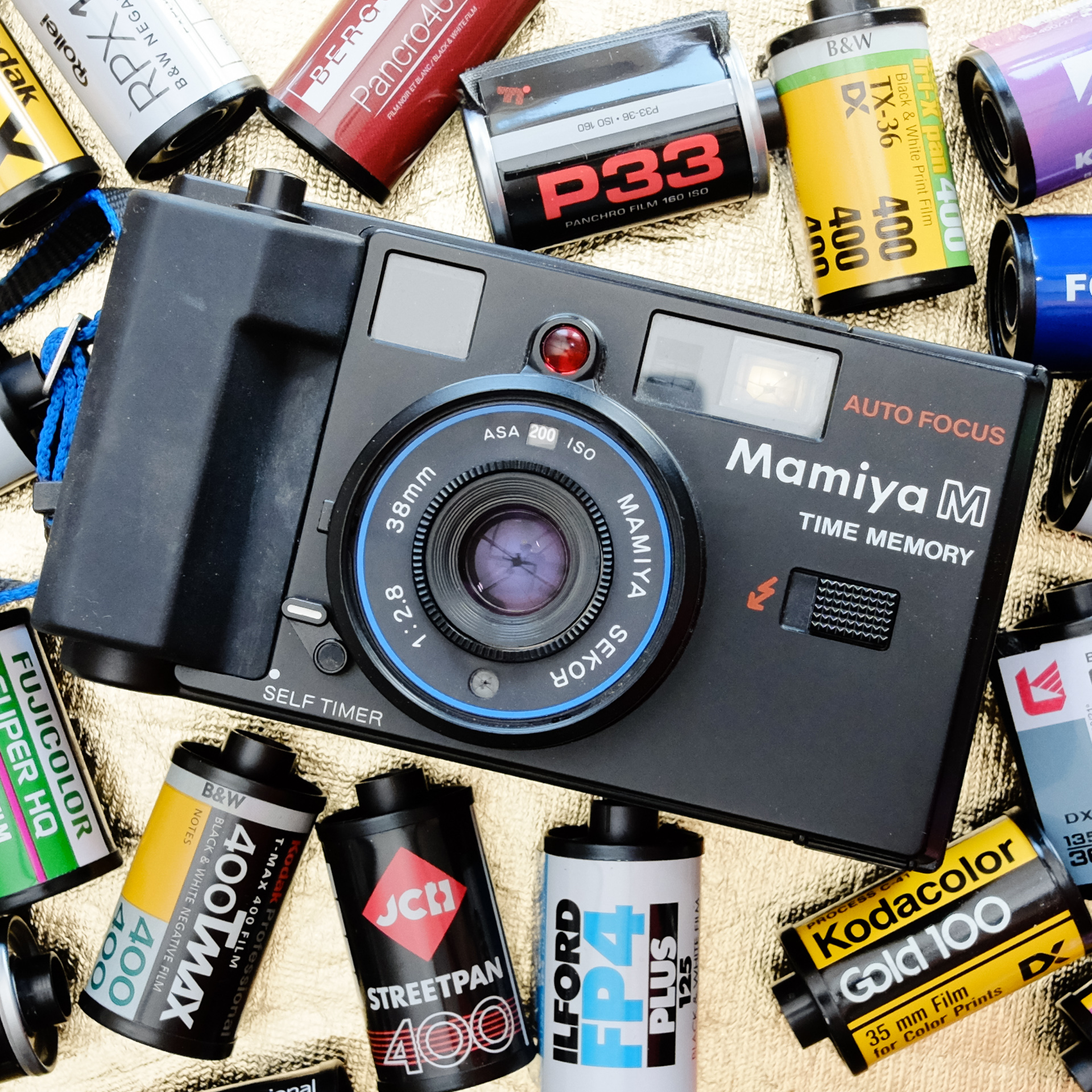 Front view of a Mamiya M Time Memory compact 35mm camera surrounded by 35mm film canisters