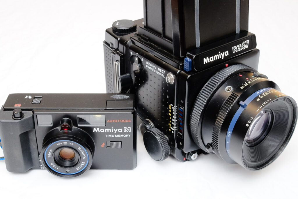 A Mamiya M Time Memory compact 35mm camera next to a Mamiya RZ67 medium format camera with a white background