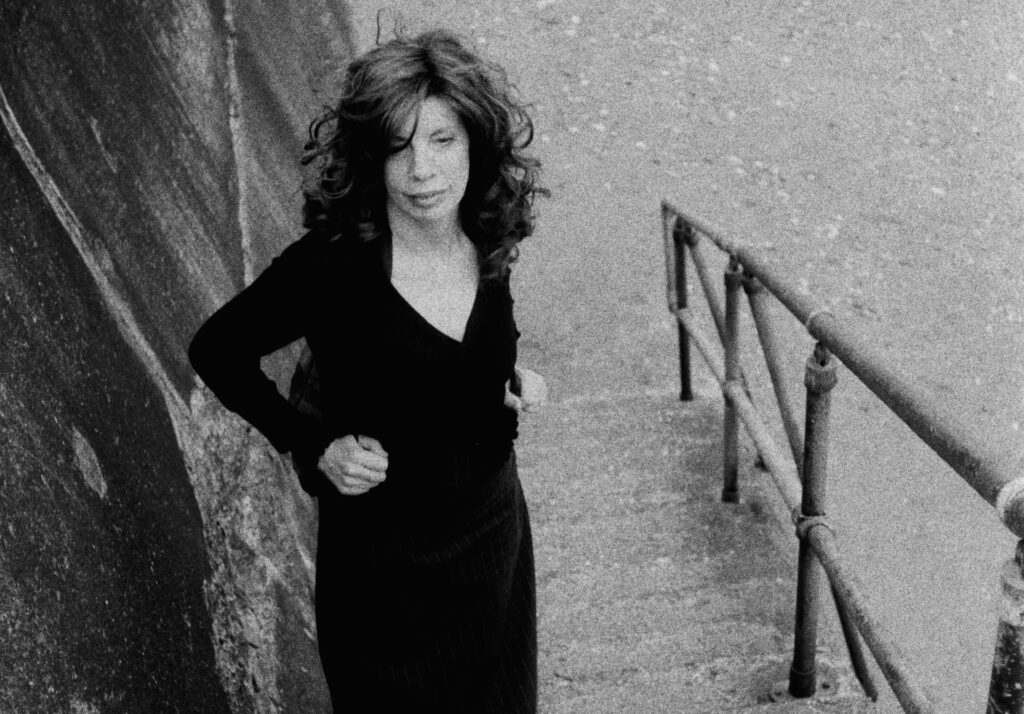 Black-and-white portrait of a woman standing by a railing in a narrow walkway, with visible grain and strong diagonal lines.