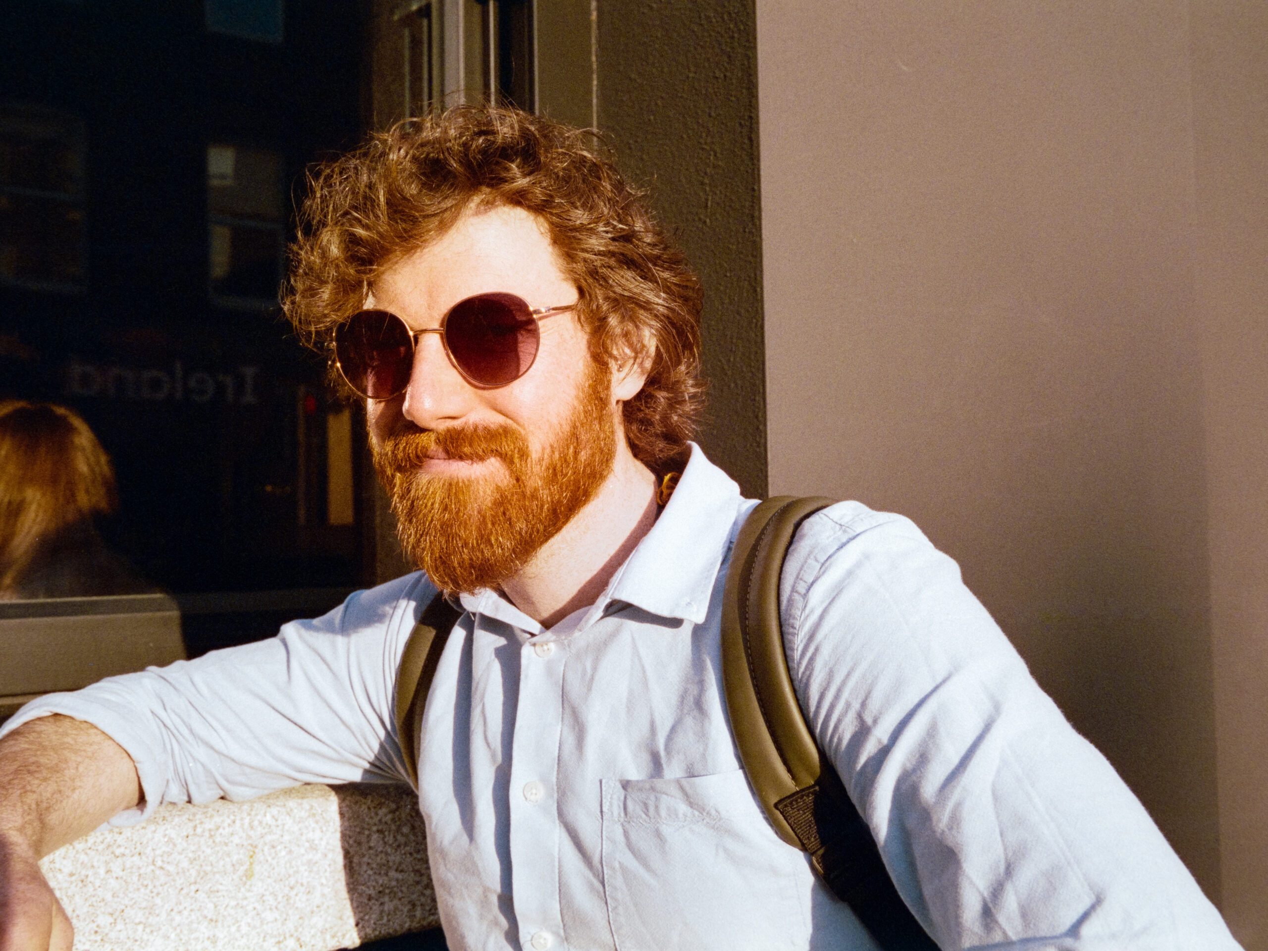 A golden hour portrait of a man with ginger hair and red sunglasses.