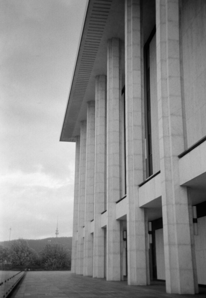 Black and white photo of the side of The National Library of Australia looking at Black Mountain and the Telstra Tower on top in the distance.