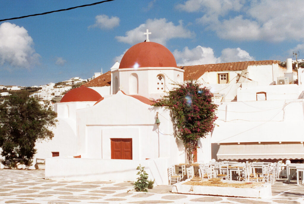 A small whitewashed church with red domes and an empty taverna with stacked chairs