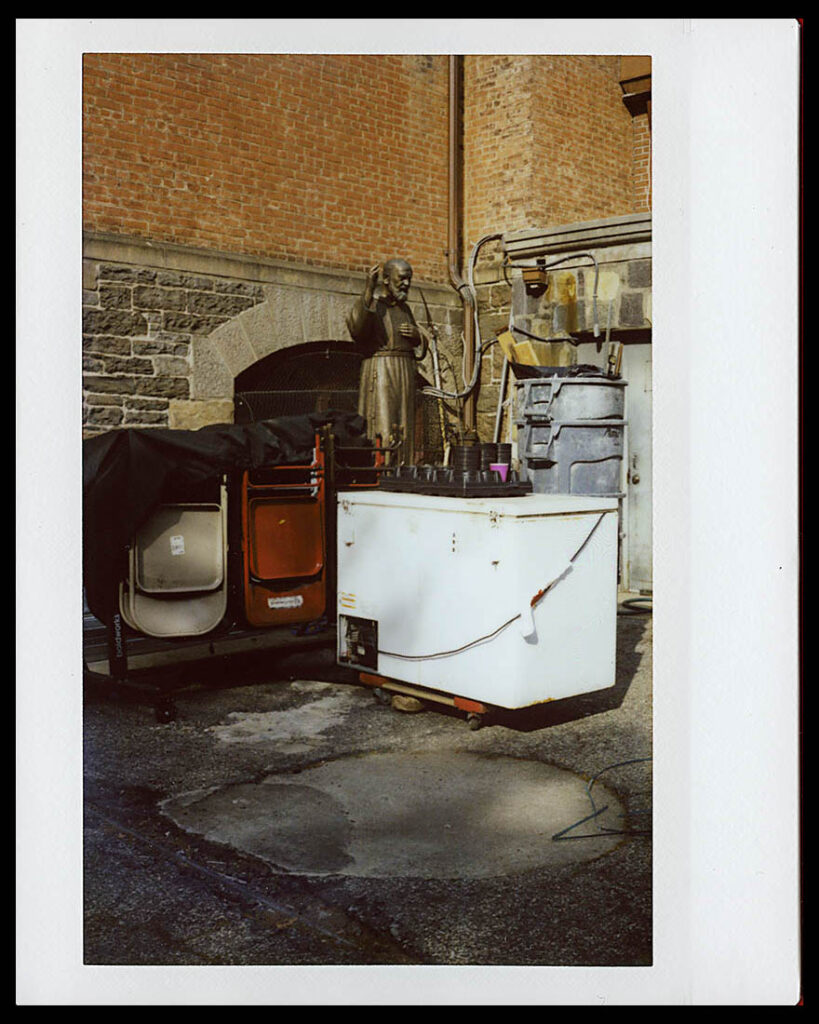 Instax Wide image showing a statue of a saint blessing what appears to be an industrial freezer.