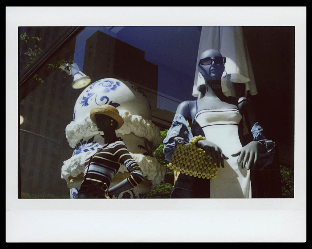 Instax Wide image of mannequins in a store window with buildings reflected in plate glass.
