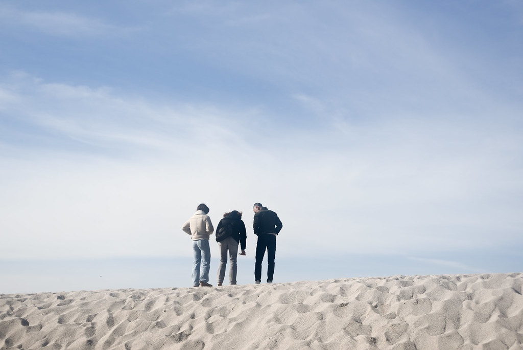Three people look from the top of the dune to the place where a sea is expected to be, but invisible
