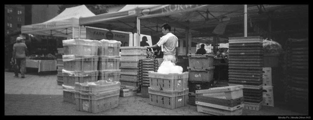 A market worker stands amidst piles of crates and bins.