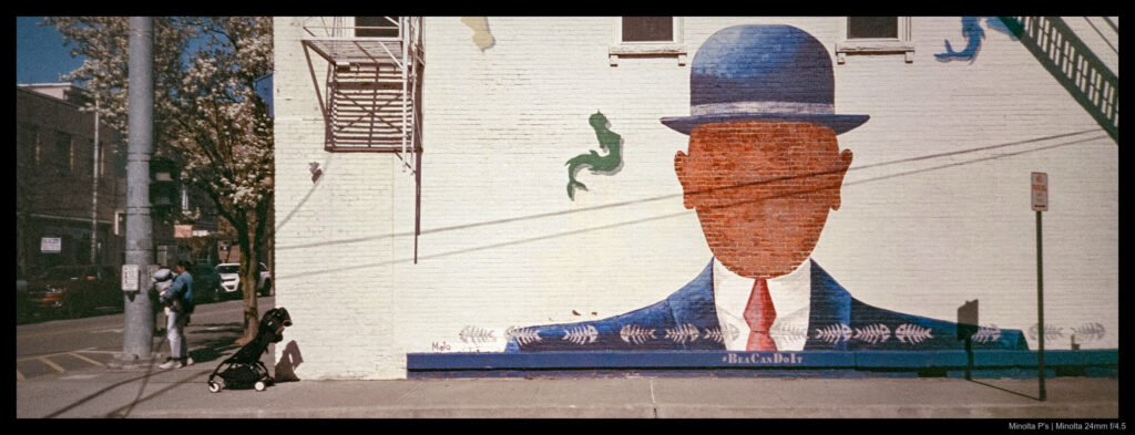 A person hits a crosswalk button under the wtachful eyes of nearby wall art.