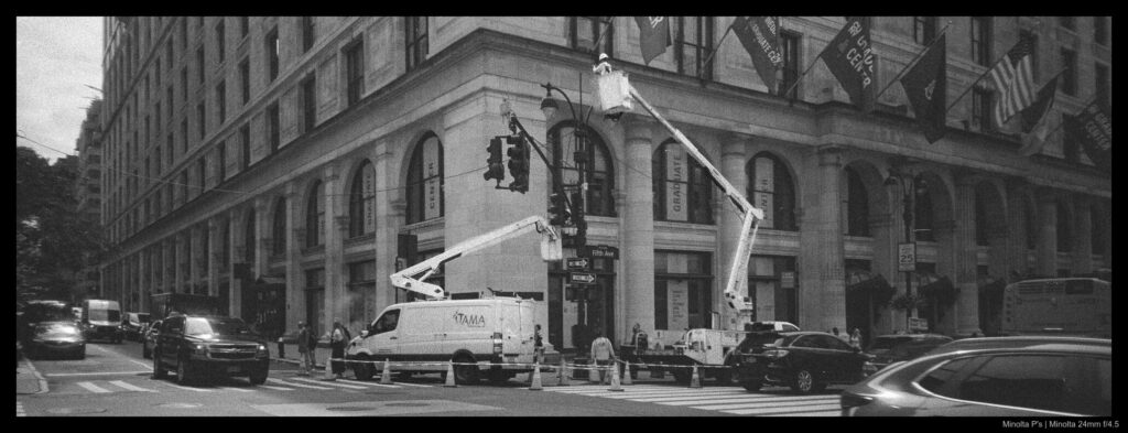 Utility workers man a wheeled crane on the corner of a street to make repairs to overhead lines.