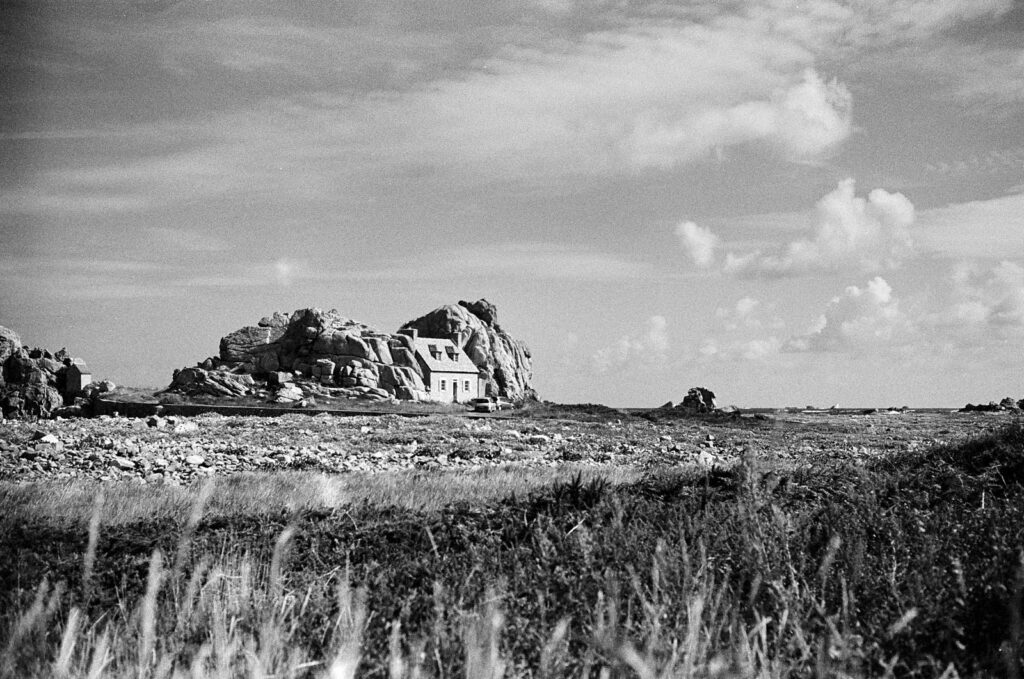 Small house among coastal rocks under a large cloudy sky, Le Gouffre near Plougrescant