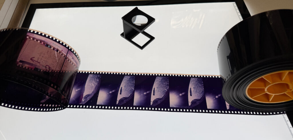 Strip of colour film transparencies on light box with magnifier