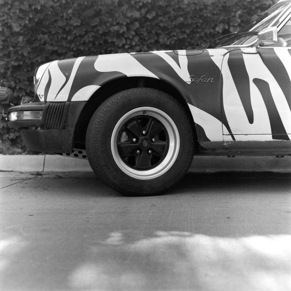 Black and white low-angle shot of the front left wheel, lifted suspension, tubular bumper, and zebra-patterned fender of a 1974 Safari Porsche 911.