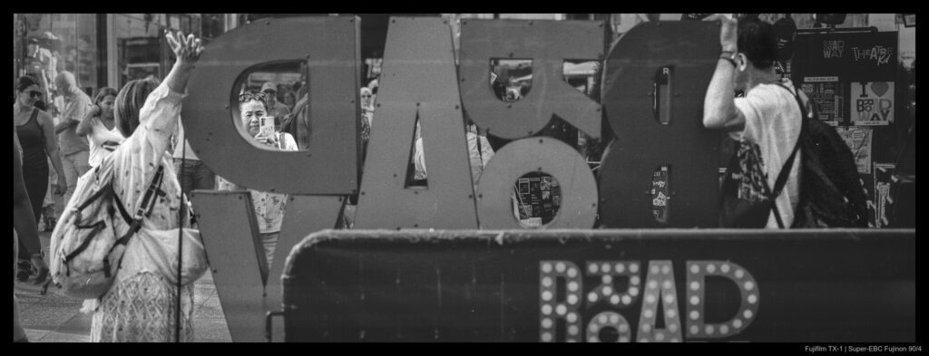 A person snaps a photo of two companions, visible through the sign they're posing by.