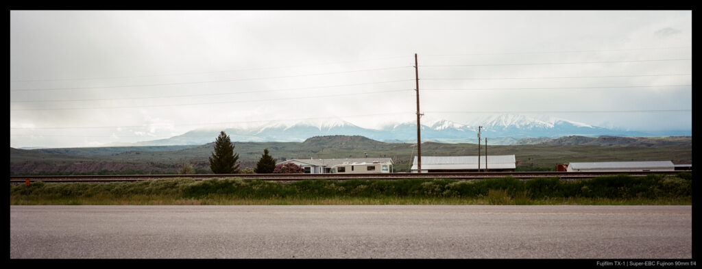An image of several low buildings on the opposite side of a highway, with distant mountains visible in the background obscured partially by low cloud cover. Snow is visible near the peak tops.
