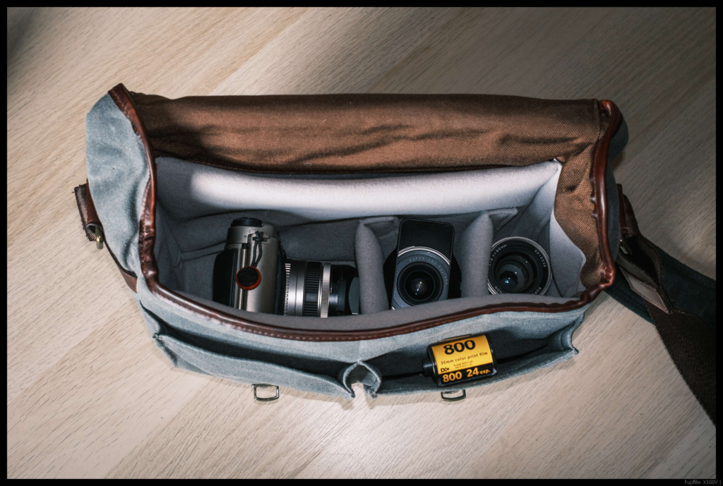 The TX-1 with the 45/4 mounted stowed alongside the 30/5.6 and 90/4 in a messenger bag, with a 135 cassette for scale. The 30/5.6 and mounted 45/4 both have their hoods attached. Note that the 45/4 and 90/4 share a hood design and the bag could have easily accommodated a third hood.