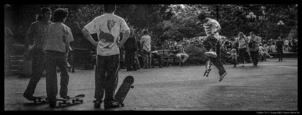 Skateboarders watch one of their own performing a trick one evening in Washington Square Park. The fading light makes both the subjects and background dim and murky.