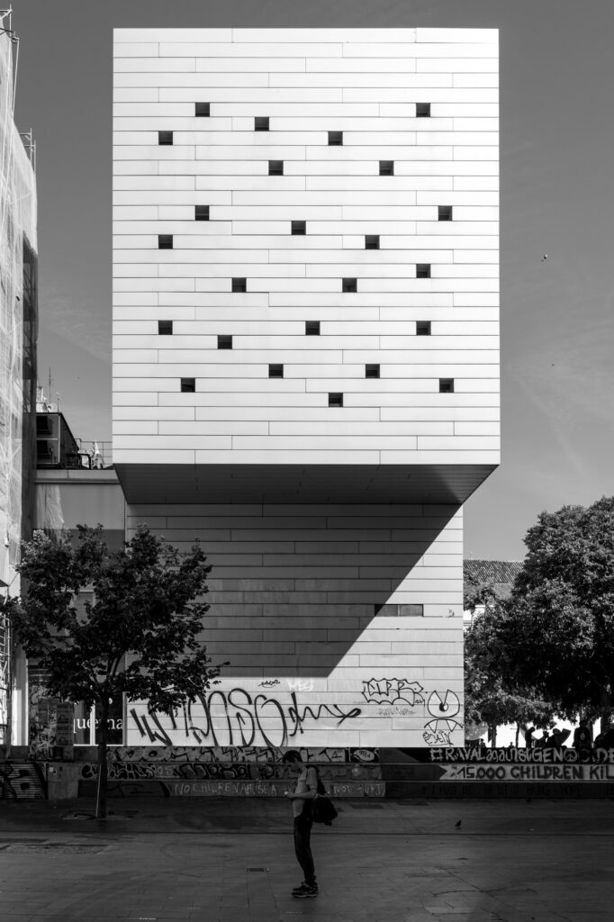 A stark white tower with scattered square windows, its graffiti-covered base overlooking the Raval