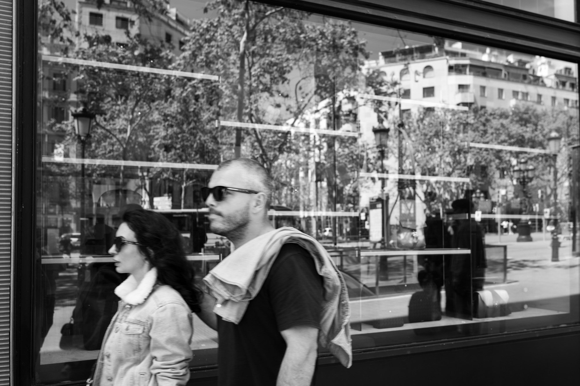 A couple reflected in a shop window along Passeig de Gràcia, city buildings visible in the glass