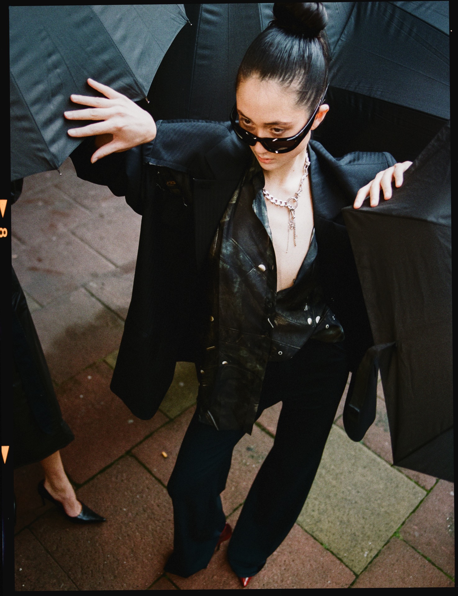 Medium format colour negative frame, fashion shot with black umbrellas on a wet pavement, film rebate and frame number visible